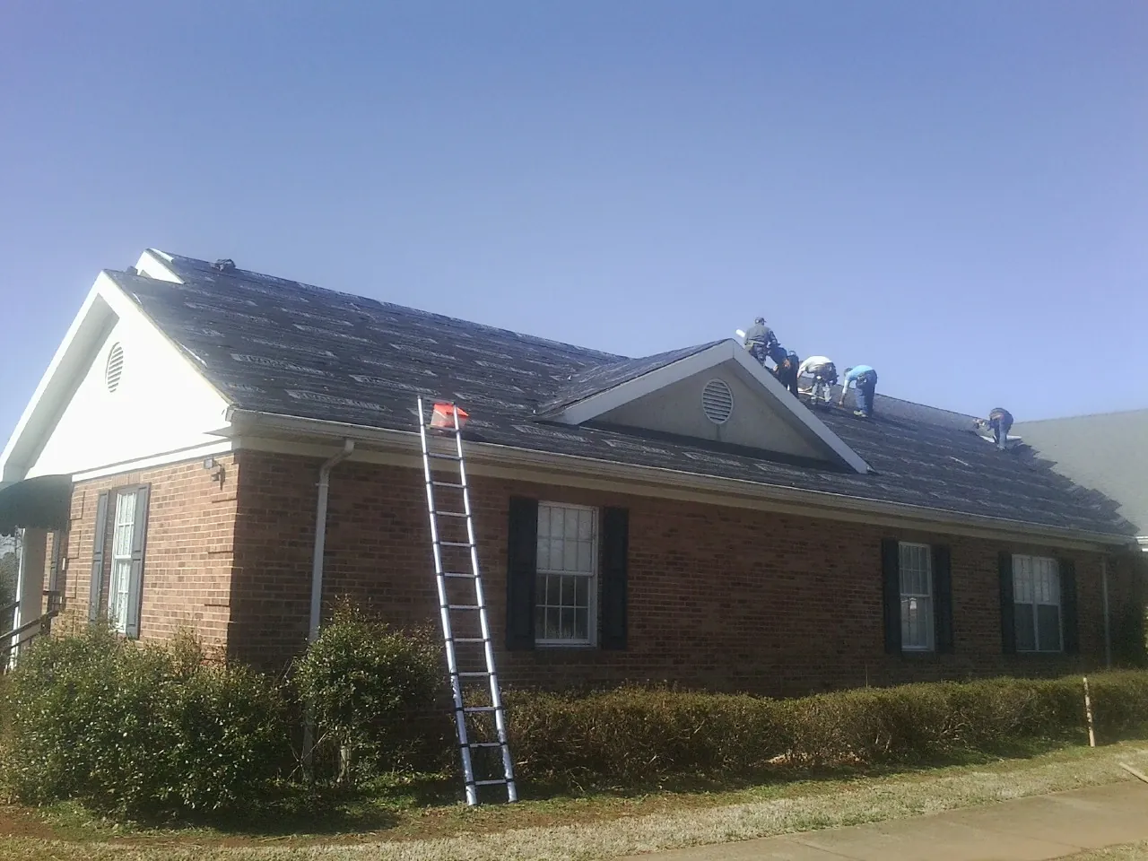 Crew tearing shingles off a brick ranch roof with a ladder set — Metal Roof Repair work by our crew in West Chester
