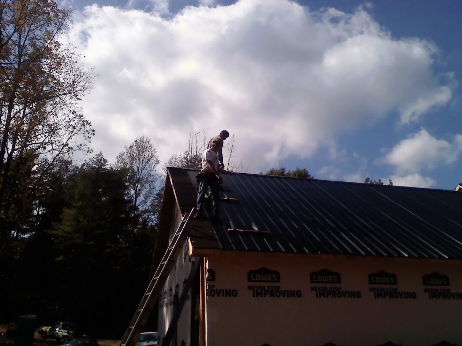 Roofer fastening dark metal panels high against a cloudy sky, from a Roof Inspection job in West Chester