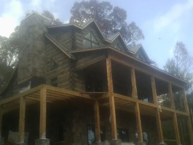 Stone chimney and dormers on a large log home with a timber porch in West Chester